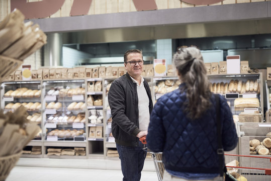 Couple talking while standing against bread rack at supermarket