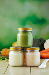 Three jars with puree with spoon near fresh fruits and vegetables