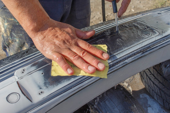 Mechanic worker repairman sanding polishing car bumper and preparing bumper for painting during repair