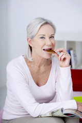 Senior woman nibbling while reading a magazine