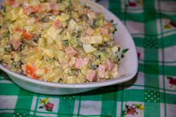 Russian traditional salad olivier with green pea, eggs, pickled cucumber, potato, sausages and mayonnaise