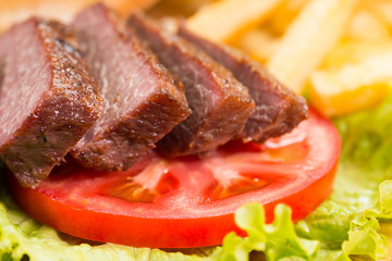 Grilled beef steaks, French fries and vegetables close-up