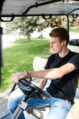 Tall handsome young man with blond hair driving a golf cart