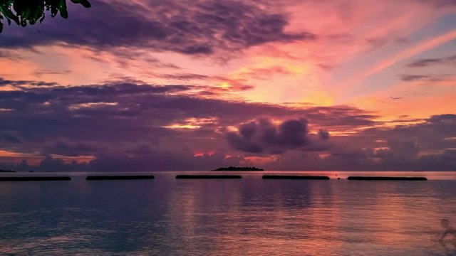 Smooth timelapse of colorful sunset on island in Maldives with orange sky, dark clouds and island at horizon. The sun sets over the horizon. Absence of people