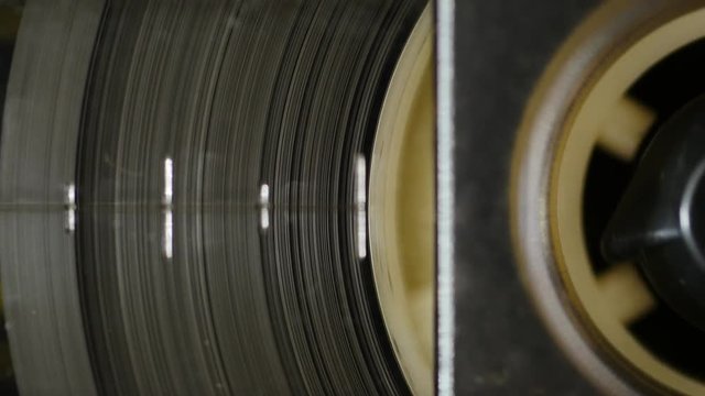 Old retro audio recorder reel spinning slowly. 4K, static macro shot. Seamless loop. Close up of audio cassette tape in use sound recording in a cassette player