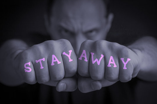 STAY AWAY written on an angry man’s fists