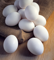 White chicken eggs wrapped in burlap next to a basket on a wooden table