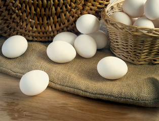 White chicken eggs wrapped in burlap next to a basket on a wooden table