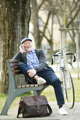 Senior man with bicycle and smart phone, making phone call