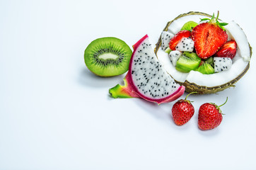 Pieces of strawberries, kiwi and dragon fruit in a half of coconut. Nearby lie two berries of strawberries, half kiwi and a slice of dragon fruit.