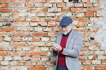 Senior man with smartphone against brick wall, texting.