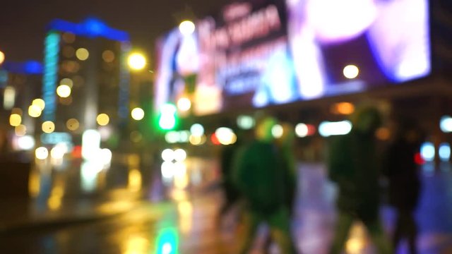 Moving color picture of the life of a big city after the rain. Going people, traveling cars, a huge billboard with animation, night street lights of a big street. Blurred image with light reflection