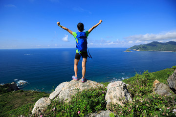 successful woman backpacker open arms on seaside mountain peak