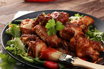 barbecue chicken wings close up on wooden tray with red spice sauce and salad