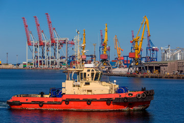 Fototapeta premium tugboat on maneuvers at seaport against background of cranes.