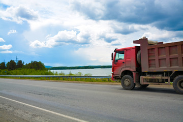 Fototapeta na wymiar A dump truck is driving along the highway in summer