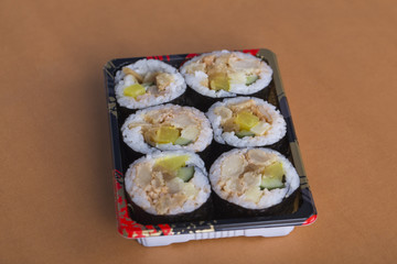 A box of sushi rolls on the yellow table.