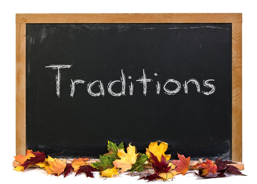 Traditions written in white chalk on a black chalkboard decorated with autumn fall leaves isolated on white