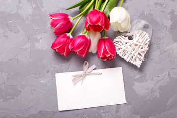 Empty tag, bright  pink  and white tulips flowers and decorative heart  on grey textured background.