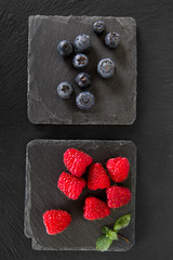 Fototapeta na wymiar raspberry and blueberries with fresh mint leaves on black slate board. 