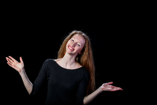 Joyful young brown-haired girl spread her hands to the sides on a black background