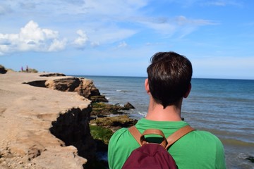 Fototapeta premium A young boy looking at the sea in the edge of a cliff