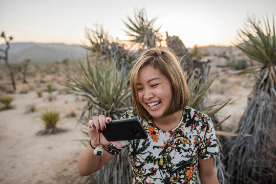 Young woman taking smartphone selfie in Joshua Tree National Park at dusk, California, USA - Powered by Adobe