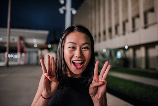 Portrait of young woman making wow hand gesture outside Los Angeles County Museum of Art at night