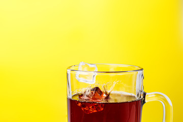 tea in transparent mug on a yellow background splashed wiht ice