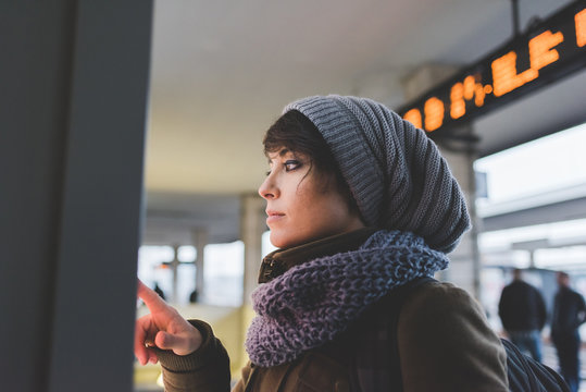 Woman in knit hat using touchscreen on railway ticket machine