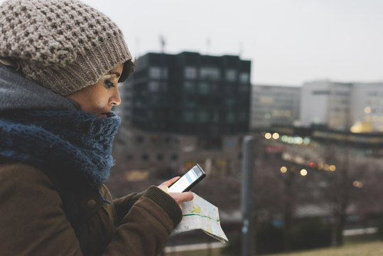 Woman in knit hat looking at smartphone in city at dusk