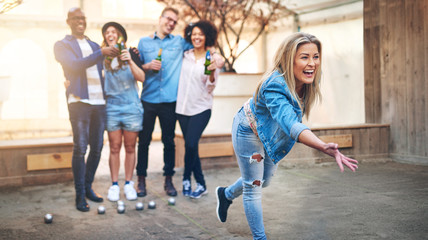 Young woman throwing petanque ball playing with friends