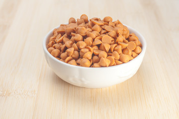 Butterscotch chips in white bowl on wooden background