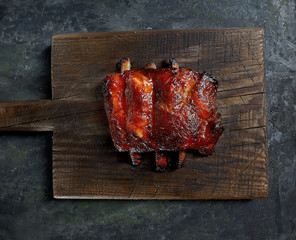 Delicious barbecued ribs seasoned with a spicy basting sauce and served with chopped fresh vegetables on an old rustic wooden chopping board in a country kitchen