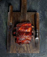 Delicious barbecued ribs seasoned with a spicy basting sauce and served with chopped fresh vegetables on an old rustic wooden chopping board in a country kitchen