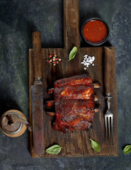 Delicious barbecued ribs seasoned with a spicy basting sauce and served with chopped fresh vegetables on an old rustic wooden chopping board in a country kitchen