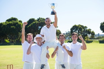 Happy cricket team with trophy standing on field
