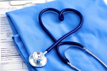 Medical stethoscope twisted in heart shape lying on patient medical history list and blue doctor uniform closeup