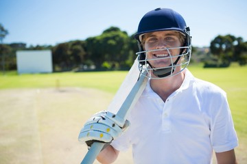 Portrait of smiling cricket player holding bat while wearing helmet