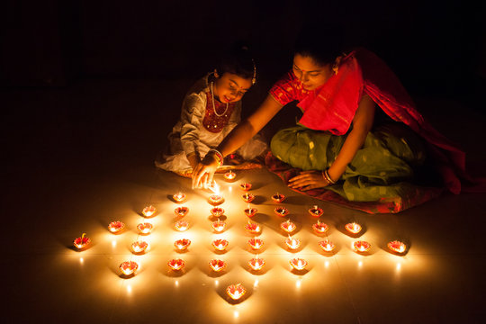 Mother and daughter lighting earthen oil lamps on Diwali