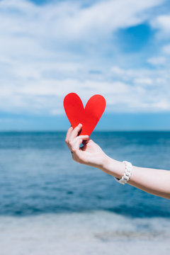 Close-up Of Woman's Hand Holding A Red Heart On The Beach