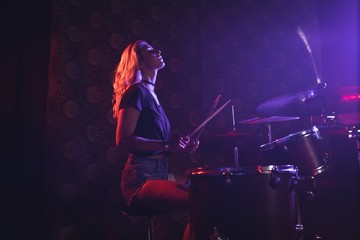 Young female drummer performing in illuminated nightclub - Powered by Adobe