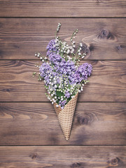Obraz na płótnie Canvas Waffle cone with lily valley and lilak flowers on wooden background