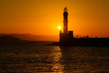 Silhouette of lighthouse in sea at sunset in the city of Chania, island of Crete, Greece. Beautiful seascape at sunset