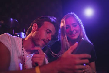 Young male and female musicians using mobile phone in nightclub