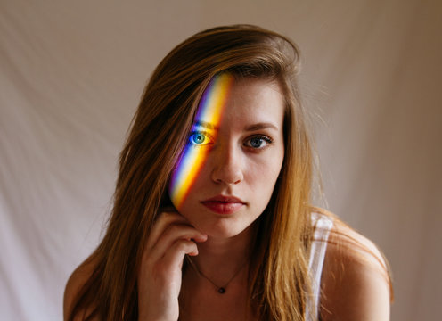 Portrait of young woman with light making rainbow stripe on face