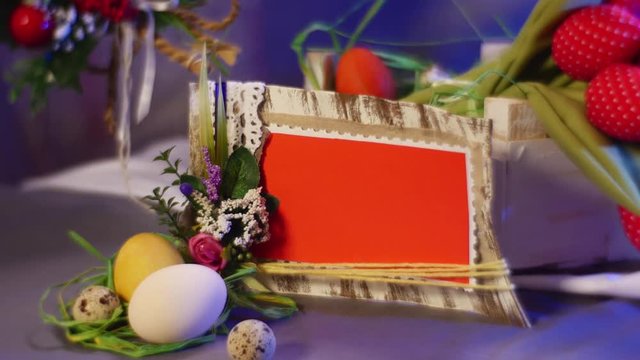 Easter Red Photo Frame is Installed Near a Wooden Kit With Red Tulips and Easter Hen and Quail Eggs Lying on a Round Table