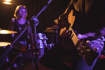 Mid section of male guitarist performing with female drummer