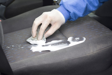 Ręka w rękawicy ochronnej pierze tapicerkę fotela samochodowego za pomocą pianki. Ręczne pranie tapicerki samochodowej za pomocą pianki do prania i gąbki. - obrazy, fototapety, plakaty