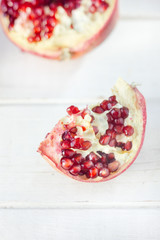 Parts of fresh pomegranate over white wooden surface.